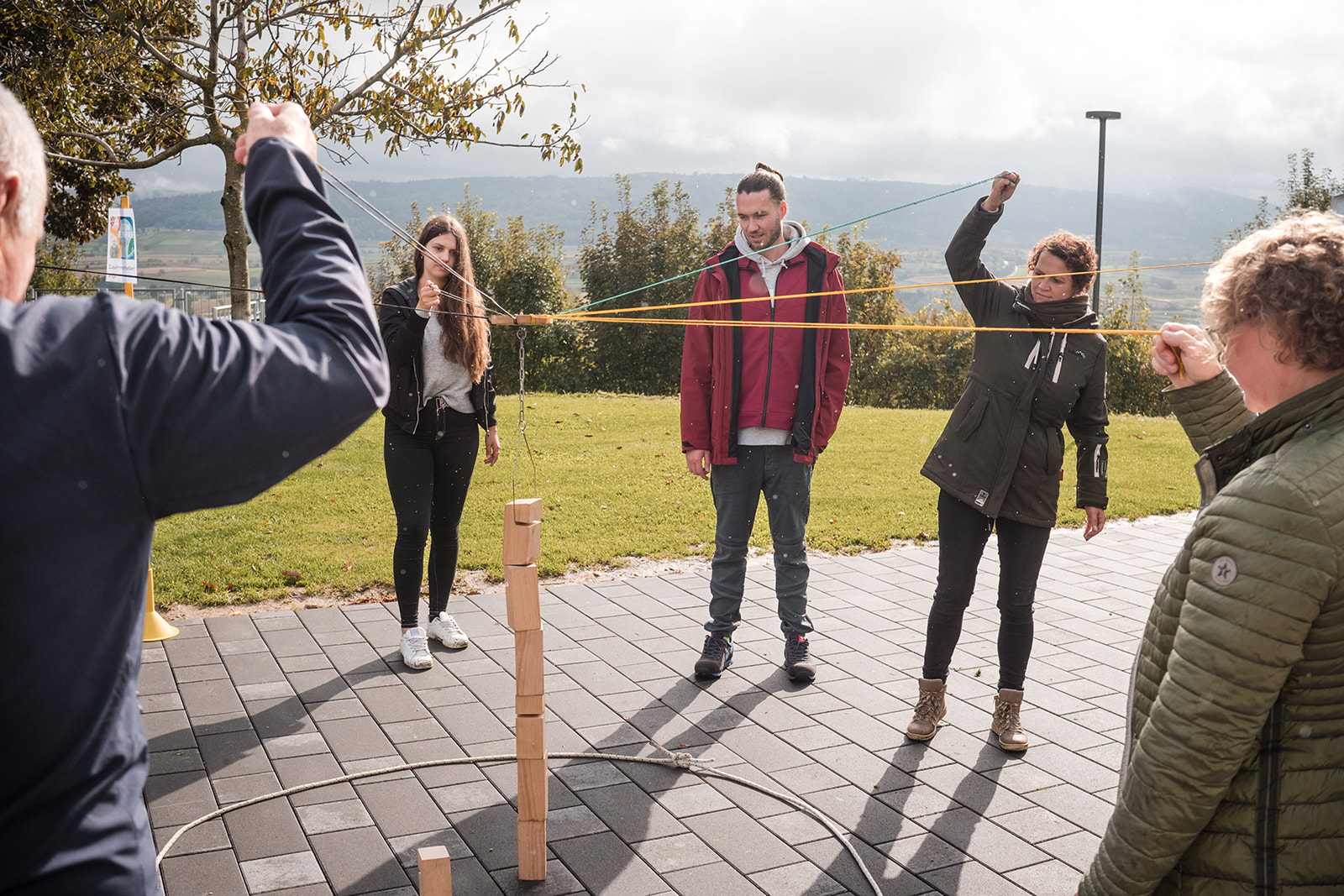Teamevent draußen: Mitarbeitende balancieren gemeinsam einen Holzquader – effektive Übung zur Förderung von Teamwork und Kommunikation.