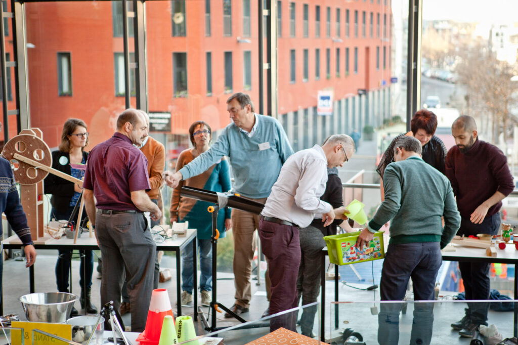 Mitarbeiter bauen gemeinsam eine Kettenreaktion während eines kreativen Teambuilding-Events in moderner Tagungslocation.