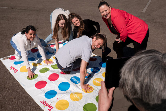 Ein Team spielt Twister bei einer Teamaktivität im Freien und lacht in die Kamera